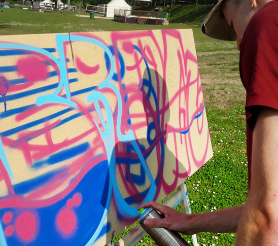 Iemand die graffiti aan het spuiten is op een plaat tijdens de workshop. Leuk voor een bedrijfsuitje, personeelsuitje, vrijgezellenfeest of een familiedag in Limburg.
