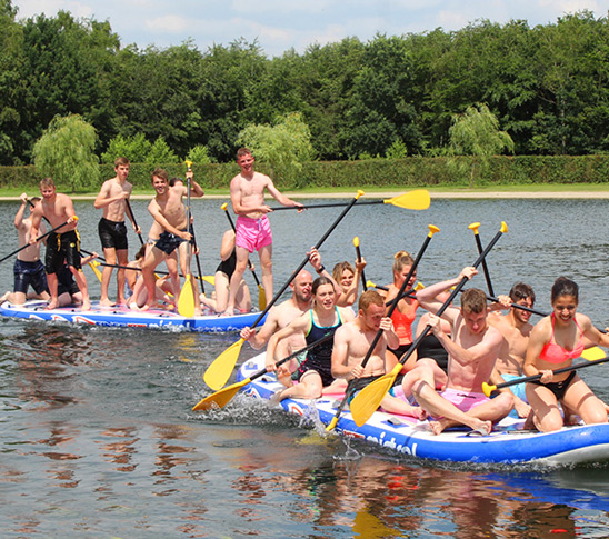 Een groep kinderen die op een grote sup op het water aan het varen zijn. Leuke activiteit voor een sportdag of schoolreisje in Midden-Limburg.