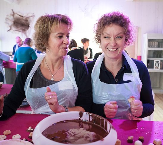 Twee dames die deelnemen aan een workshop waarbij ze van gesmolten chocola bonbons gaan maken.