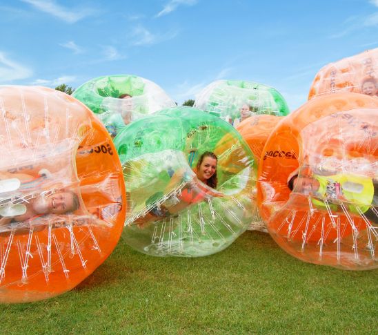 Actieve foto van een bubble voetbal activiteit waarbij deelnemers in grote opblaasbare ballen over het gras rollen en tegen elkaar botsen. De afbeelding verbeeldt een speelse en energieke groepsactiviteit vol actie, lachen en teamwork binnen een group event.