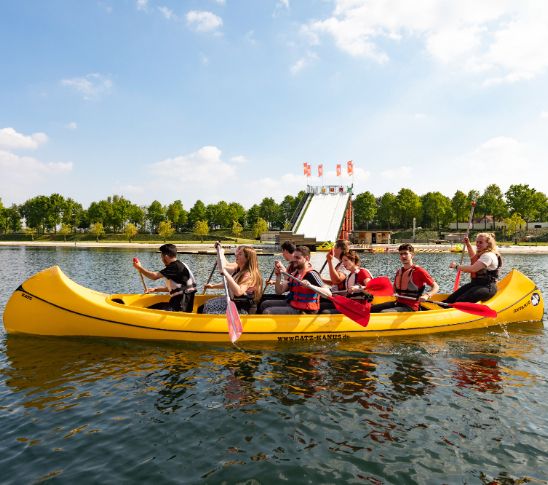 Actieve foto van een groep deelnemers die samen in een kano over het water peddelen. De afbeelding verbeeldt een sportieve en samenwerkende groepsactiviteit waarbij teamwork, communicatie en plezier centraal staan binnen een group event.