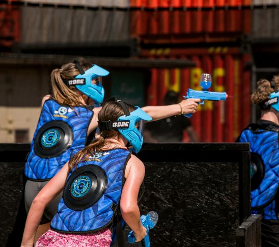 Actieve foto van een lasergame-achtige groepsactiviteit waarbij deelnemers beschermende maskers dragen en elkaar met gelpistolen proberen te raken. De afbeelding verbeeldt een dynamische en competitieve groepsactiviteit vol actie, strategie en teamwork binnen een group event.