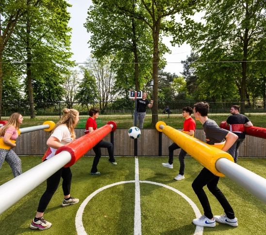 Actieve foto van een potje tafelvoetbal in levensgroot formaat, waarbij teams tegenover elkaar staan en samen de stangen bedienen om te scoren. De afbeelding verbeeldt een speelse en sportieve groepsactiviteit waarin samenwerking, competitie en plezier centraal staan binnen een group event.